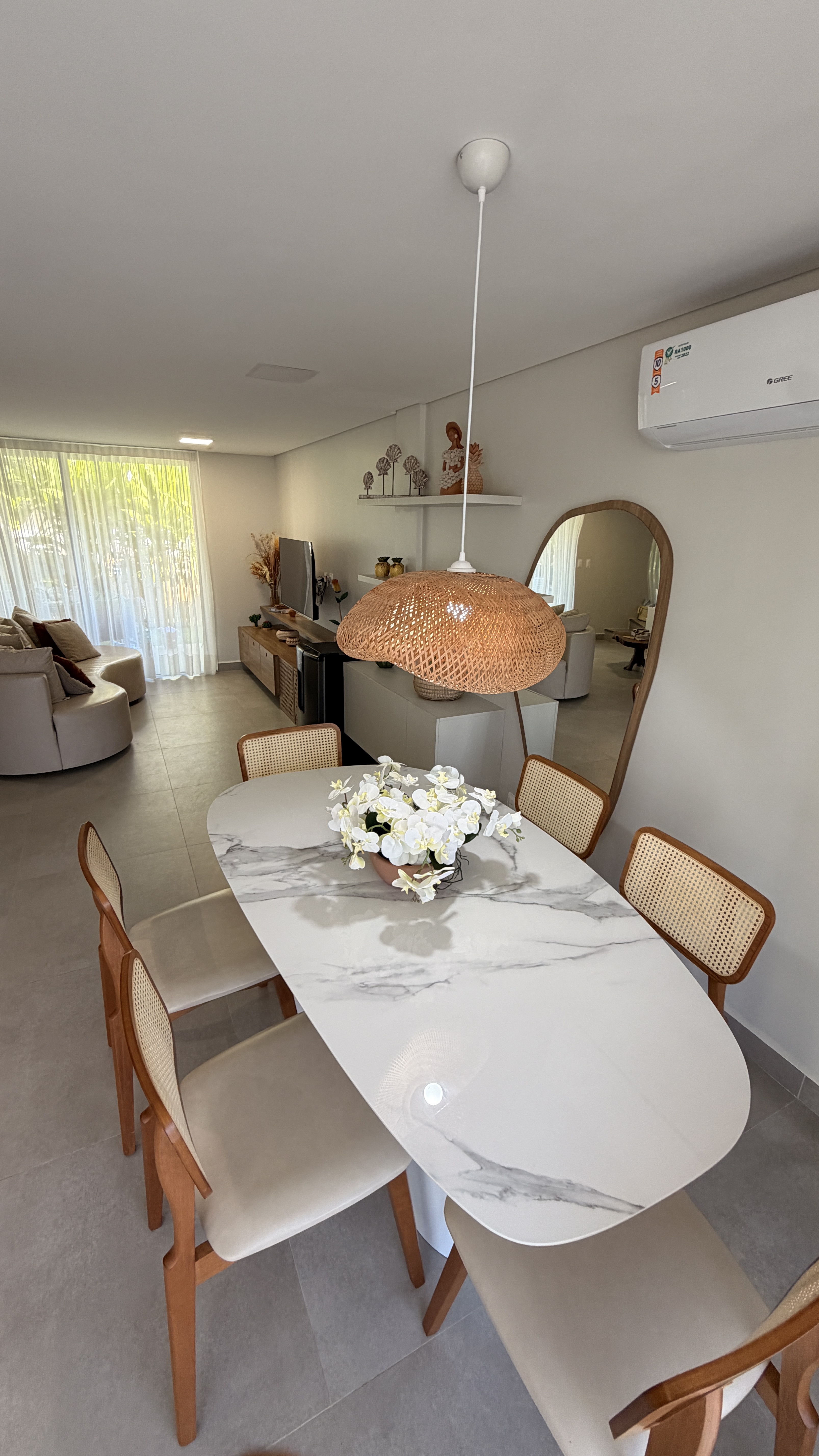 Área de jantar com mesa oval, cadeiras de madeira e luminária de fibra natural