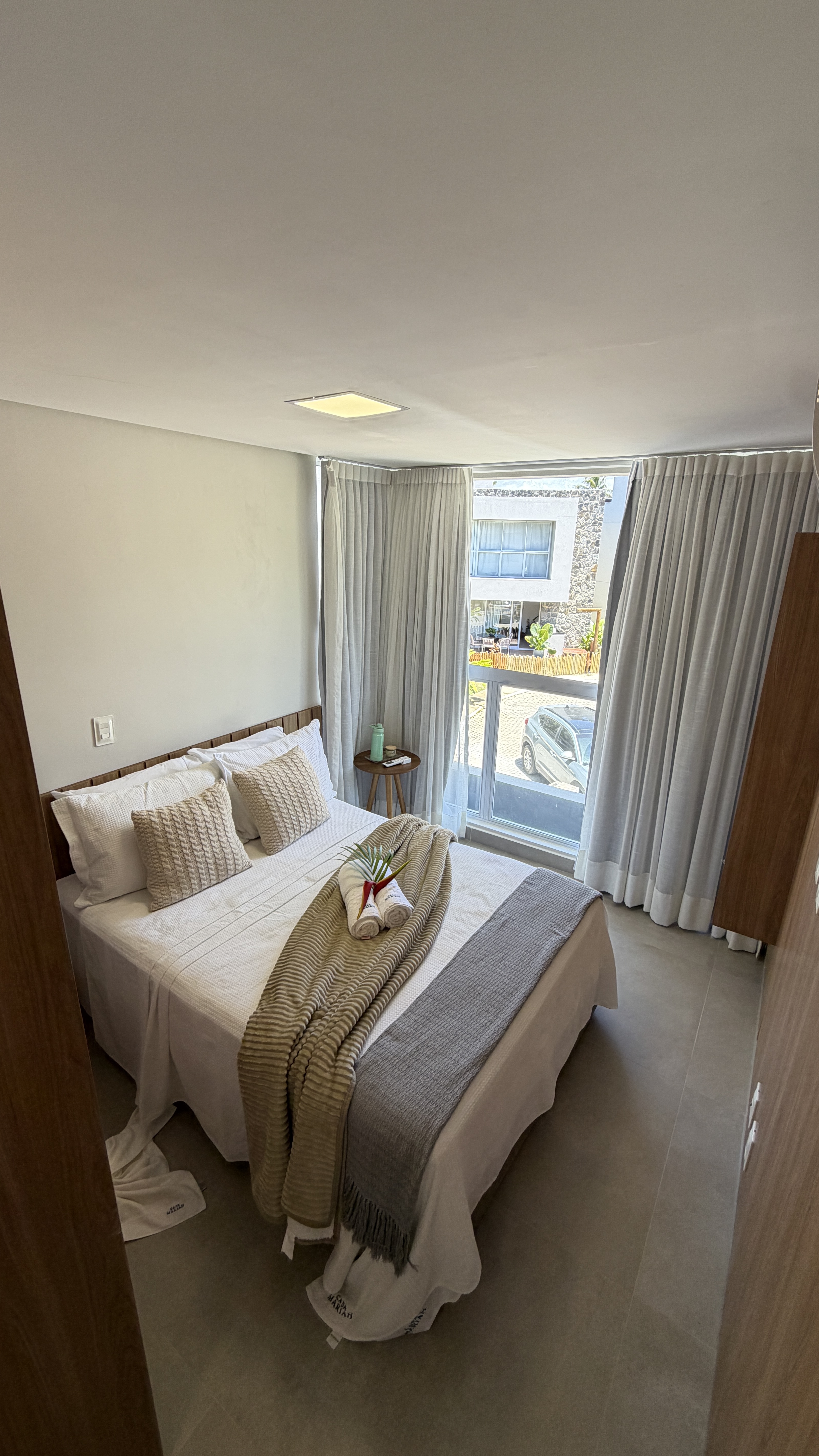 Quarto de casal com roupa de cama em tons neutros e janela ampla